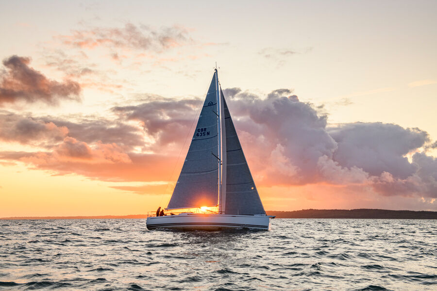 Ein Segelboot der Marke Arcona segelt bei Sonnenuntergang auf ruhiger See unter einem farbenfrohen Himmel.