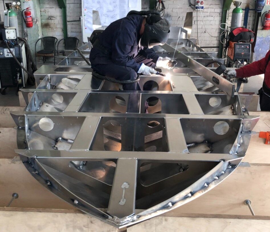 Ein Arbeiter verschweisst das Metallgeruest eines Aluminiumbootes in einer Produktionshalle.