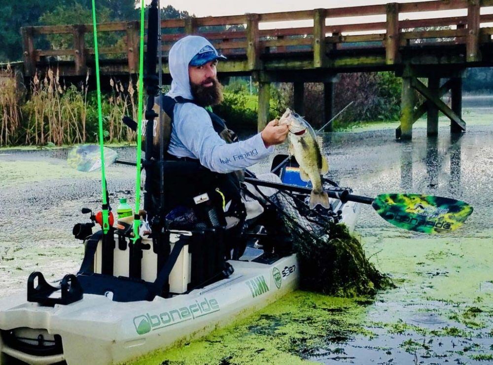 Ein Angler sitzt auf einem Bonafide Angelkajak und hält stolz einen frisch gefangenen Fisch in die Höhe.
