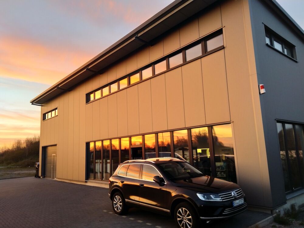 Ein modernes Firmengebäude im warmen Licht des Sonnenuntergangs mit einem geparkten SUV davor.