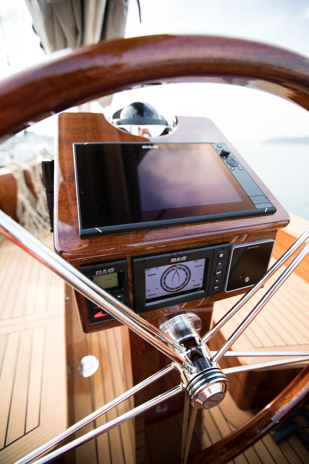 Blick durch das Steuerrad auf eine edle Schiffssteuerung aus Holz mit integrierten B&G-Displays.