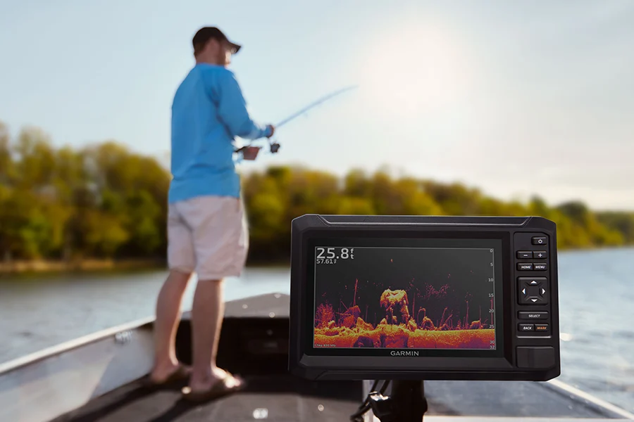Ein Garmin Echolot zeigt Unterwasserstrukturen auf dem Bildschirm, während im Hintergrund ein Mann auf einem Boot angelt.