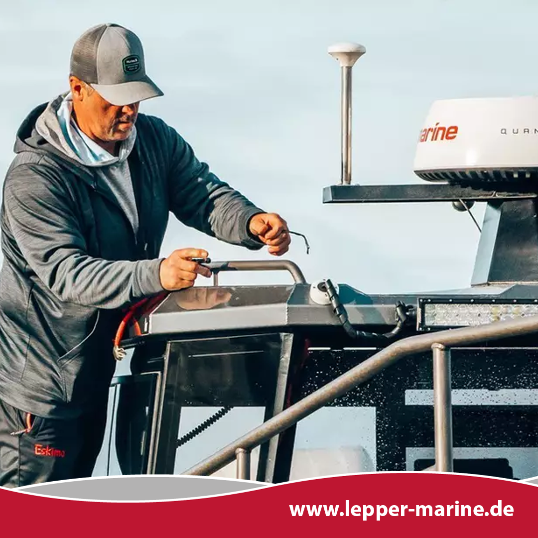 Ein Mann in Funktionskleidung arbeitet an der Verkabelung und Ausrüstung auf dem Dach eines Bootes.